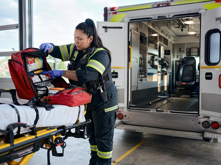 A paramedic restocking a trauma kit beside an ambulance.