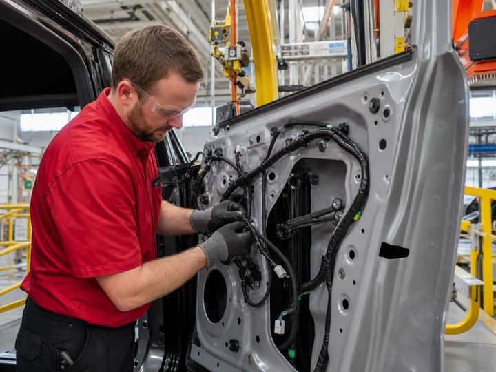 An automotive assembly worker installing electrical components on a vehicle door.