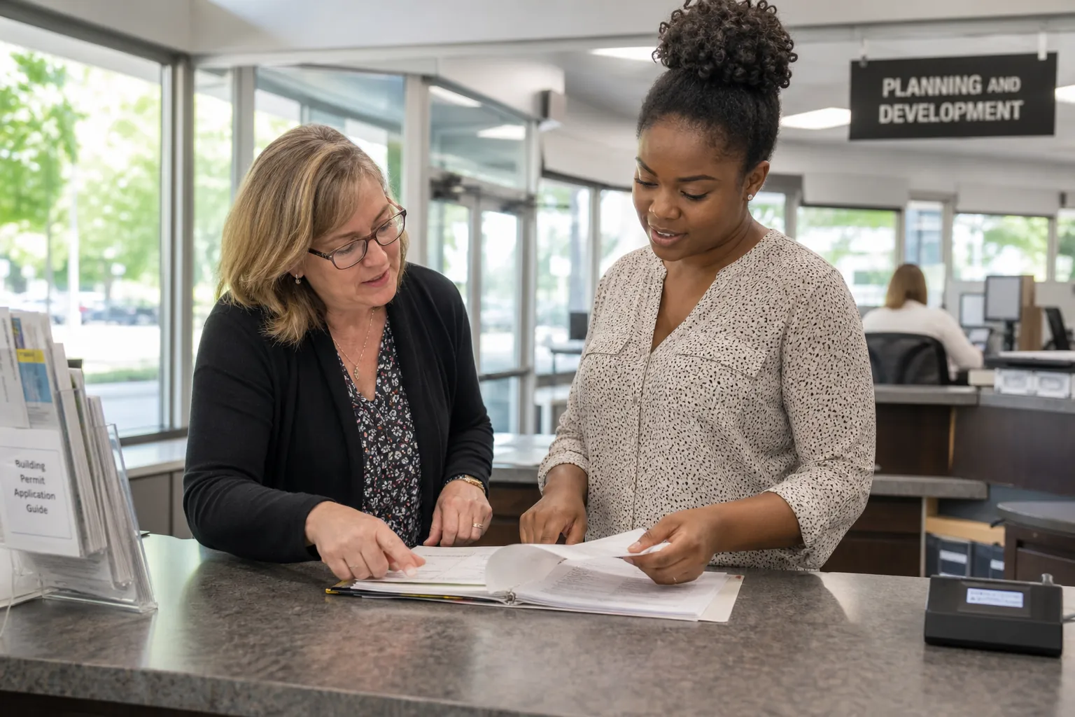 Clerical staff reviewing files at a bright public-service counter.