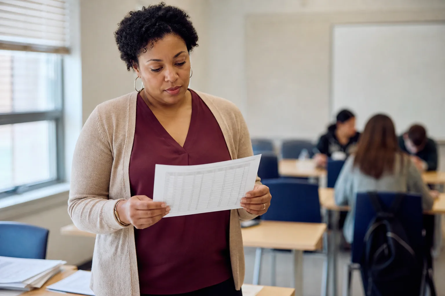 Office: educator (a white woman) and office admin check a roster against the schedule on a monitor.